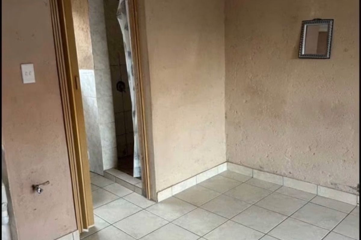 An empty bedroom featuring tiled flooring and direct access to an en-suite bathroom with a shower.