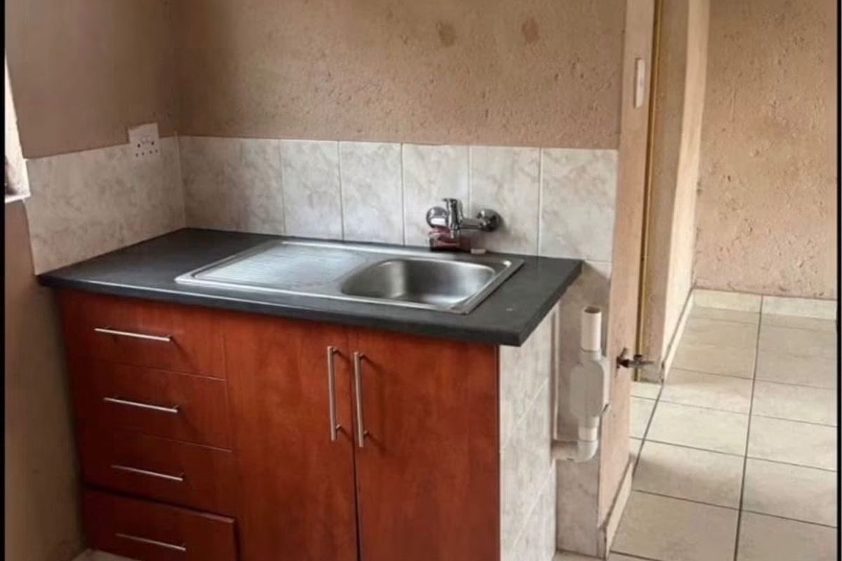 A compact kitchen area featuring a single sink unit with built-in cabinetry, tiled flooring, and a tiled splashback, requiring cosmetic updates.