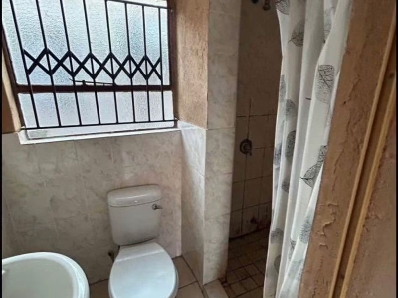 A functional bathroom featuring a pedestal basin, toilet, and shower area with tiled finishes and a security-fitted window.