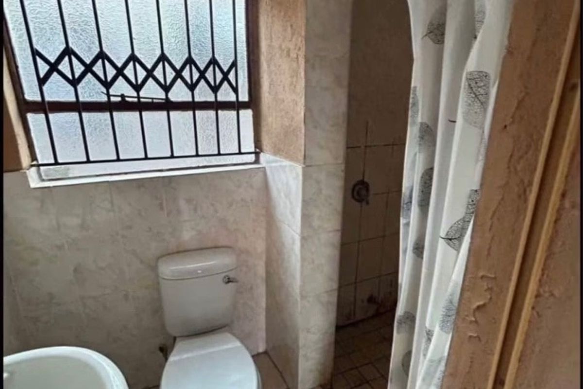 A functional bathroom featuring a pedestal basin, toilet, and shower area with tiled finishes and a security-fitted window.