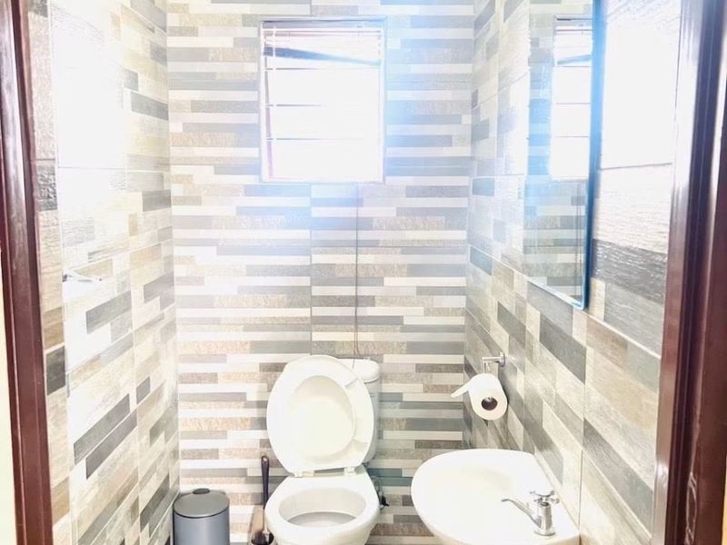 A compact guest bathroom featuring floor-to-ceiling tiled walls, a wall-mounted basin, and a standard toilet.