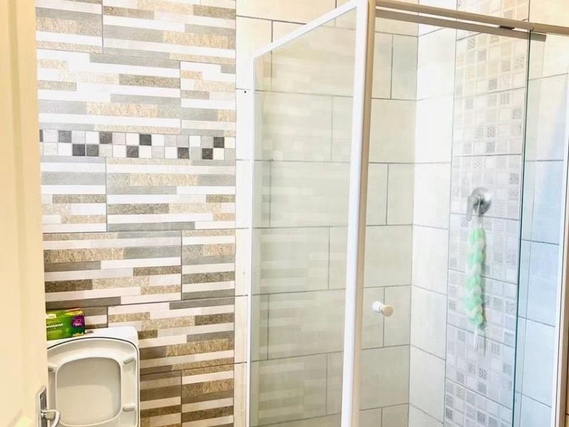 A modern bathroom featuring a glass-enclosed shower with a rainfall shower head and decorative tiled wall accents.