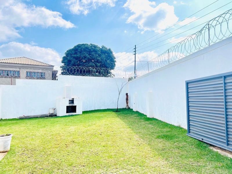 A private backyard garden featuring a lawn, a built-in braai, and high perimeter walls secured with razor wire.