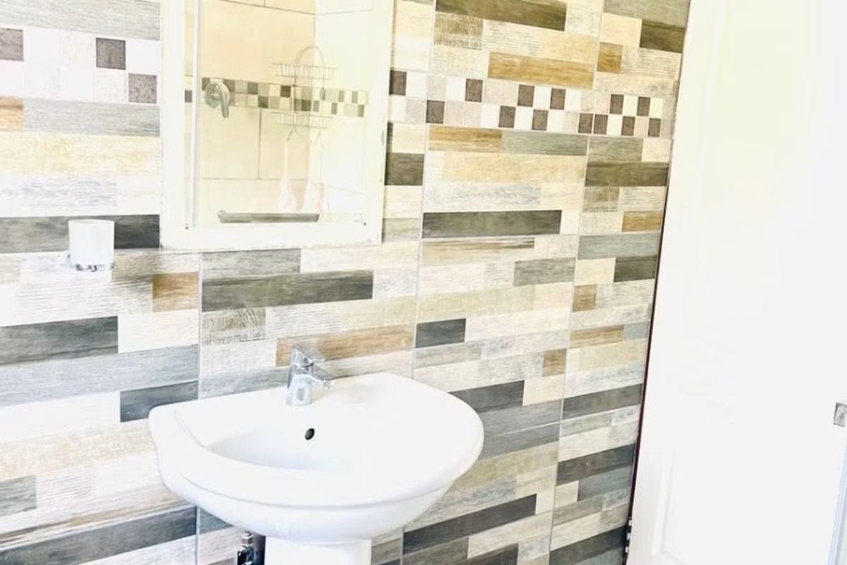 A clean bathroom featuring a white pedestal basin, wall-mounted mirror, and decorative multi-toned wall tiling.
