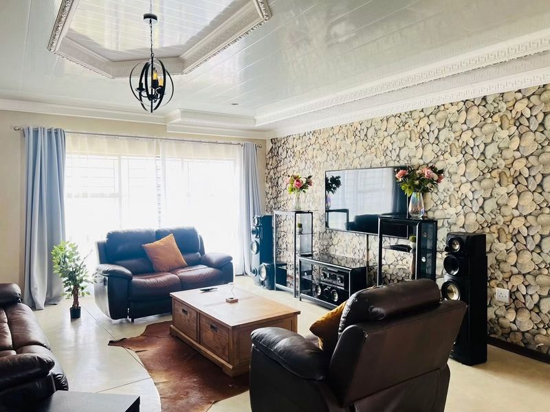 Spacious living room featuring a distinctive stone-clad feature wall, elegant coffered ceiling with recessed lighting, and large windows allowing for ample natural light.