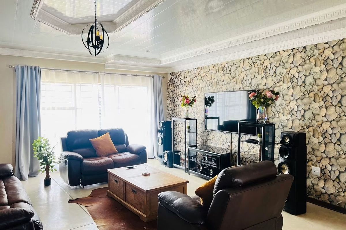 Spacious living room featuring a distinctive stone-clad feature wall, elegant coffered ceiling with recessed lighting, and large windows allowing for ample natural light.