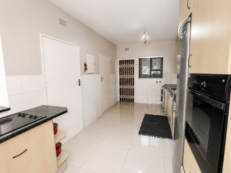 A functional kitchen featuring light wood cabinetry, granite countertops, built-in oven and hob, tiled flooring, and a secure rear entrance.