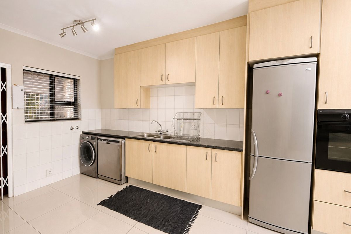 A functional kitchen featuring light-wood cabinetry, black granite countertops, a double sink, and built-in oven, complemented by neutral tiled flooring and backsplash.