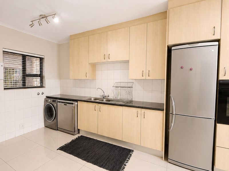 A functional kitchen featuring light-wood cabinetry, black granite countertops, a double sink, and built-in oven, complemented by neutral tiled flooring and backsplash.