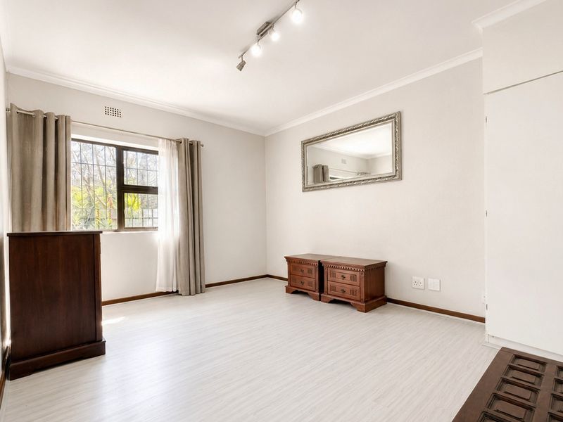 A bright and spacious bedroom featuring light-toned laminate flooring, built-in storage, and security bars on the window.