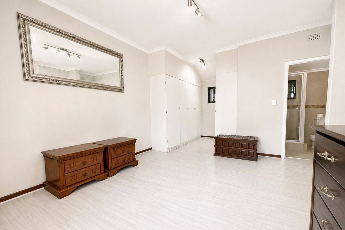 Spacious bedroom featuring light laminate flooring, ample built-in cupboard storage, and an en-suite bathroom access.