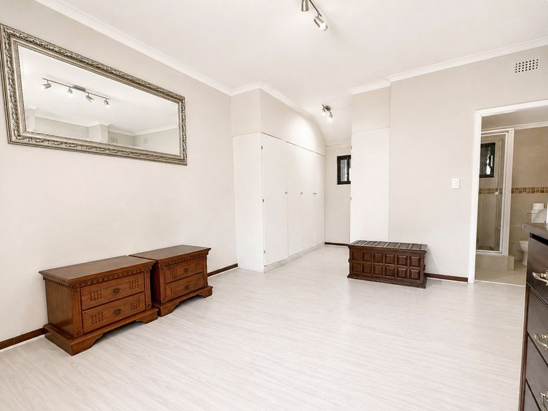 Spacious bedroom featuring light laminate flooring, ample built-in cupboard storage, and an en-suite bathroom access.