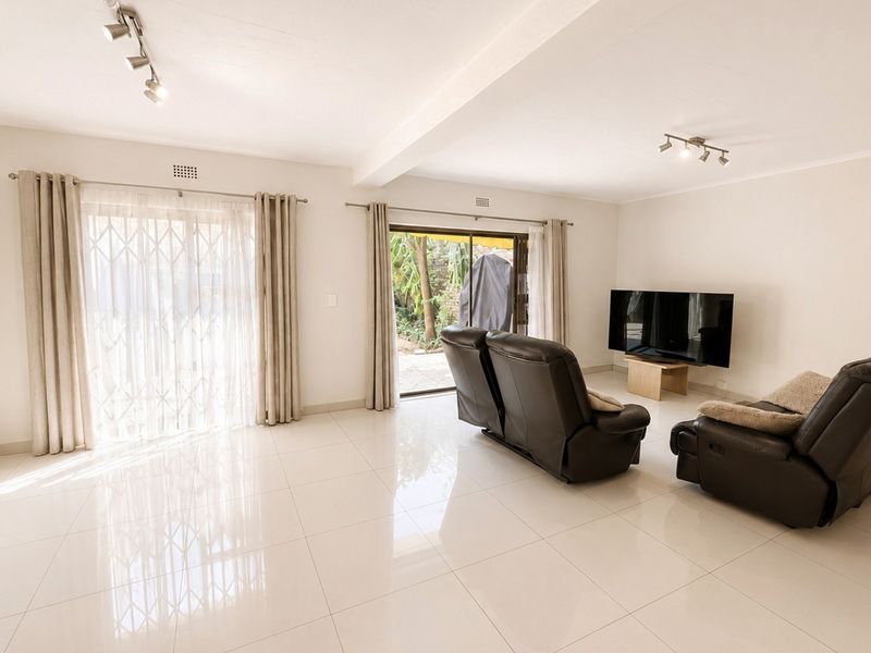 Spacious living room featuring polished tile flooring, track lighting, and dual sliding glass doors providing access to the outdoor area.