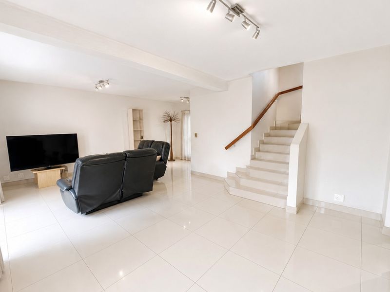 Spacious open-plan living area featuring polished tile flooring, modern track lighting, and a central staircase with a wooden handrail.