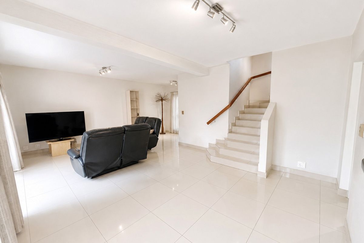 Spacious open-plan living area featuring polished tile flooring, modern track lighting, and a central staircase with a wooden handrail.