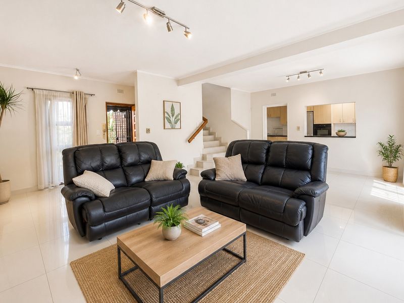 Spacious open-plan living area featuring polished tile flooring, a central staircase, and a convenient pass-through window connecting to the kitchen.