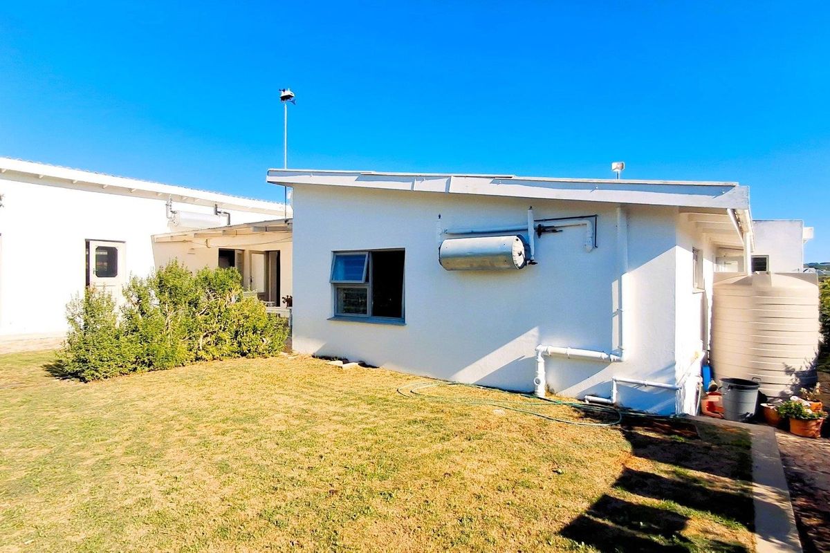 Rear exterior view of the property featuring a white facade, solar water heating system, and a large water storage tank set against a lawn.