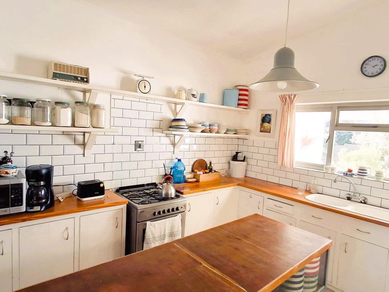 A bright kitchen featuring white subway tile backsplash, wooden countertops, open shelving, and a gas stove, offering a functional and classic aesthetic.