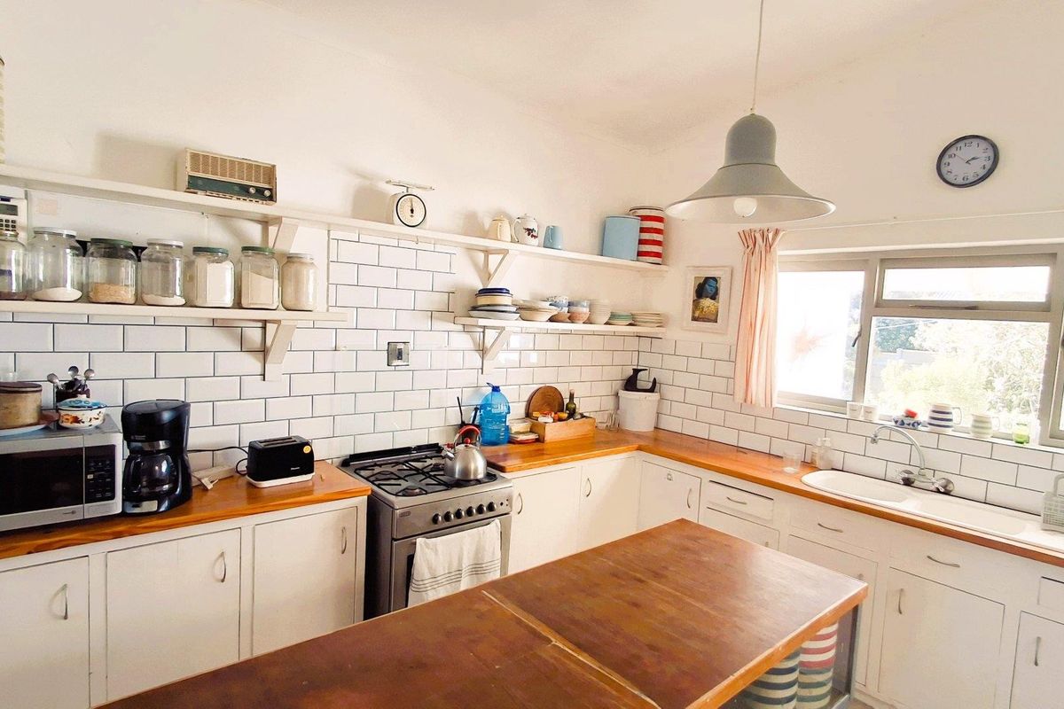 A bright kitchen featuring white subway tile backsplash, wooden countertops, open shelving, and a gas stove, offering a functional and classic aesthetic.