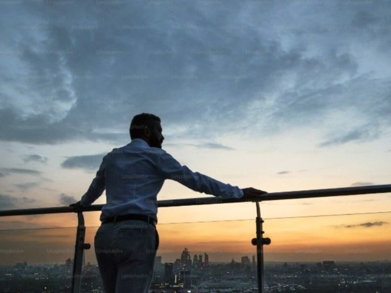 A scenic elevated view of the city skyline at sunset, featuring a modern glass and metal balustrade.