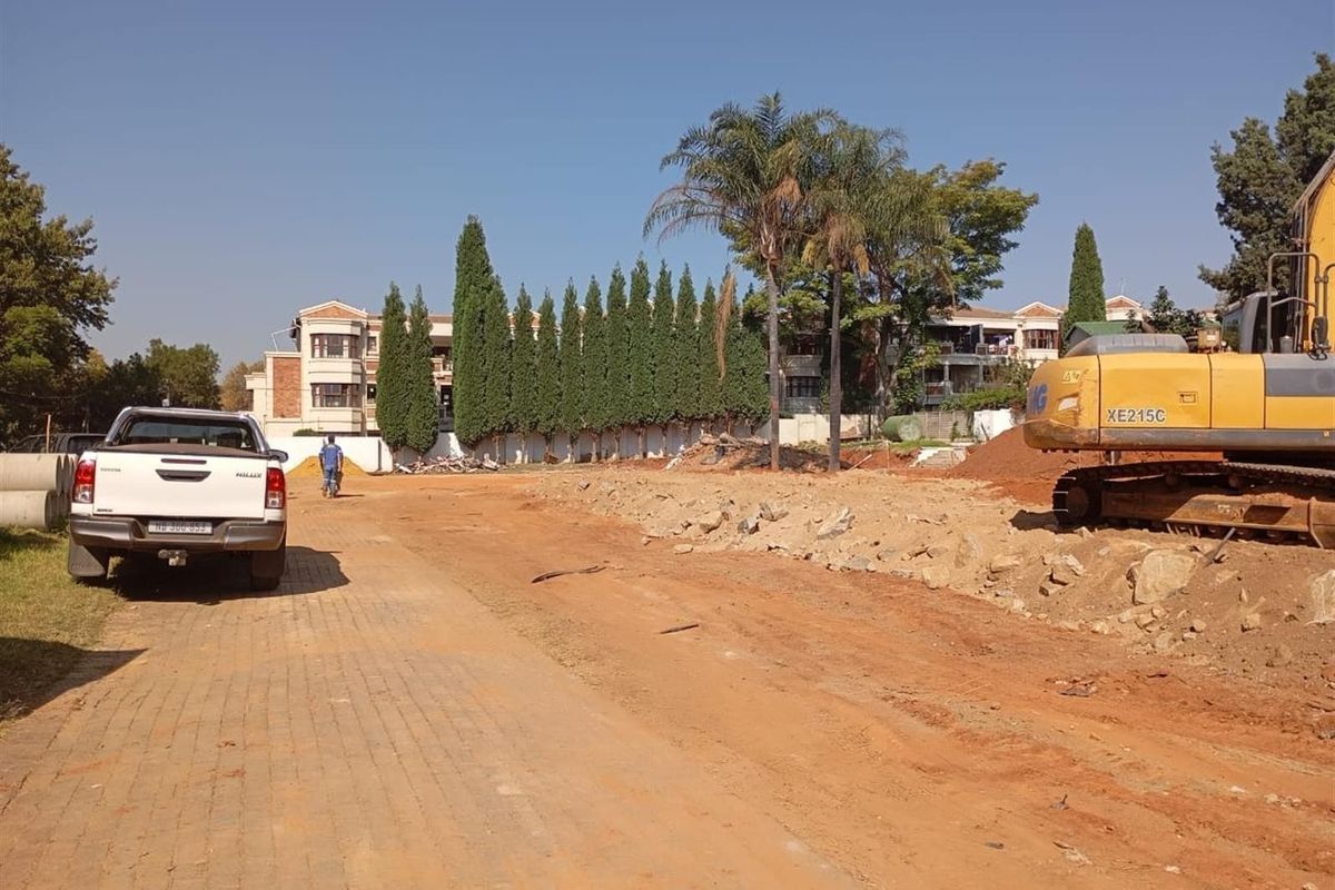 An exterior view of a property under construction, featuring a paved driveway, surrounding trees, and heavy machinery on site.