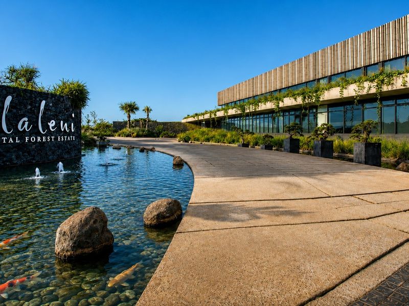 A beautifully landscaped entrance to Elaleni Coastal Forest Estate, featuring a modern architectural facade, a serene koi pond, and a paved driveway.