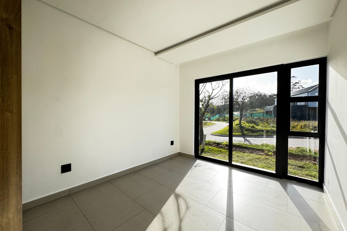 A bright, empty living area featuring large format floor tiles and a modern black aluminium sliding door with views of the garden.