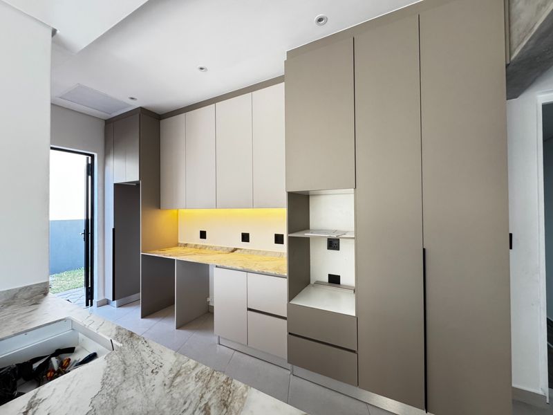 Modern scullery featuring sleek built-in cabinetry, stone countertops, and integrated under-cabinet lighting, providing a clean and functional secondary kitchen or utility space.