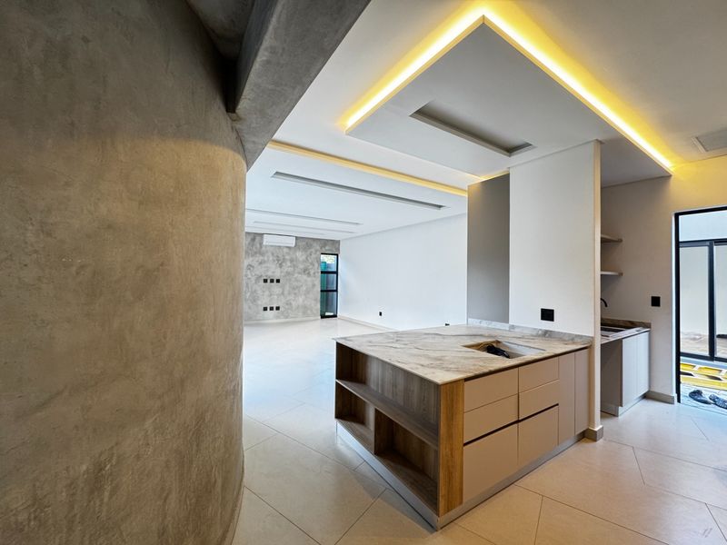 Modern open-plan living area featuring a sleek kitchen island with stone countertops, recessed ceiling lighting, and a striking concrete feature wall.