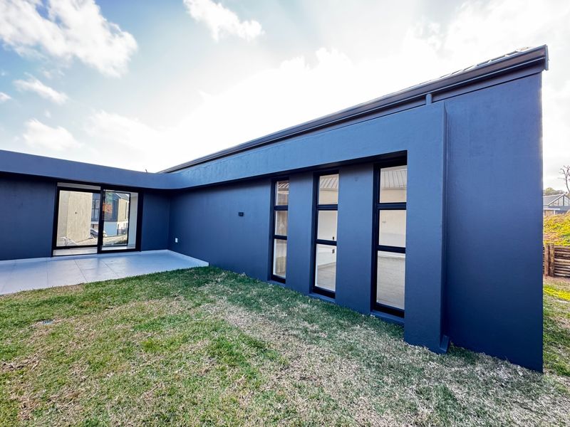 Modern rear exterior view featuring dark painted walls, large windows, sliding glass doors, and a paved patio area overlooking the garden.
