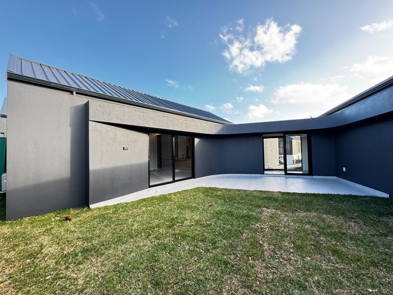 A modern rear exterior view featuring a tiled patio, dark rendered walls, and large sliding glass doors opening into the home.