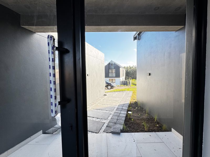 A view from the entrance looking out towards a modern paved walkway and landscaped garden area between two contemporary building structures.
