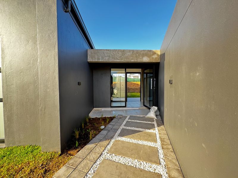 Modern front entrance featuring a paved walkway with stone accents, dark grey exterior walls, and glass sliding doors leading into the home.