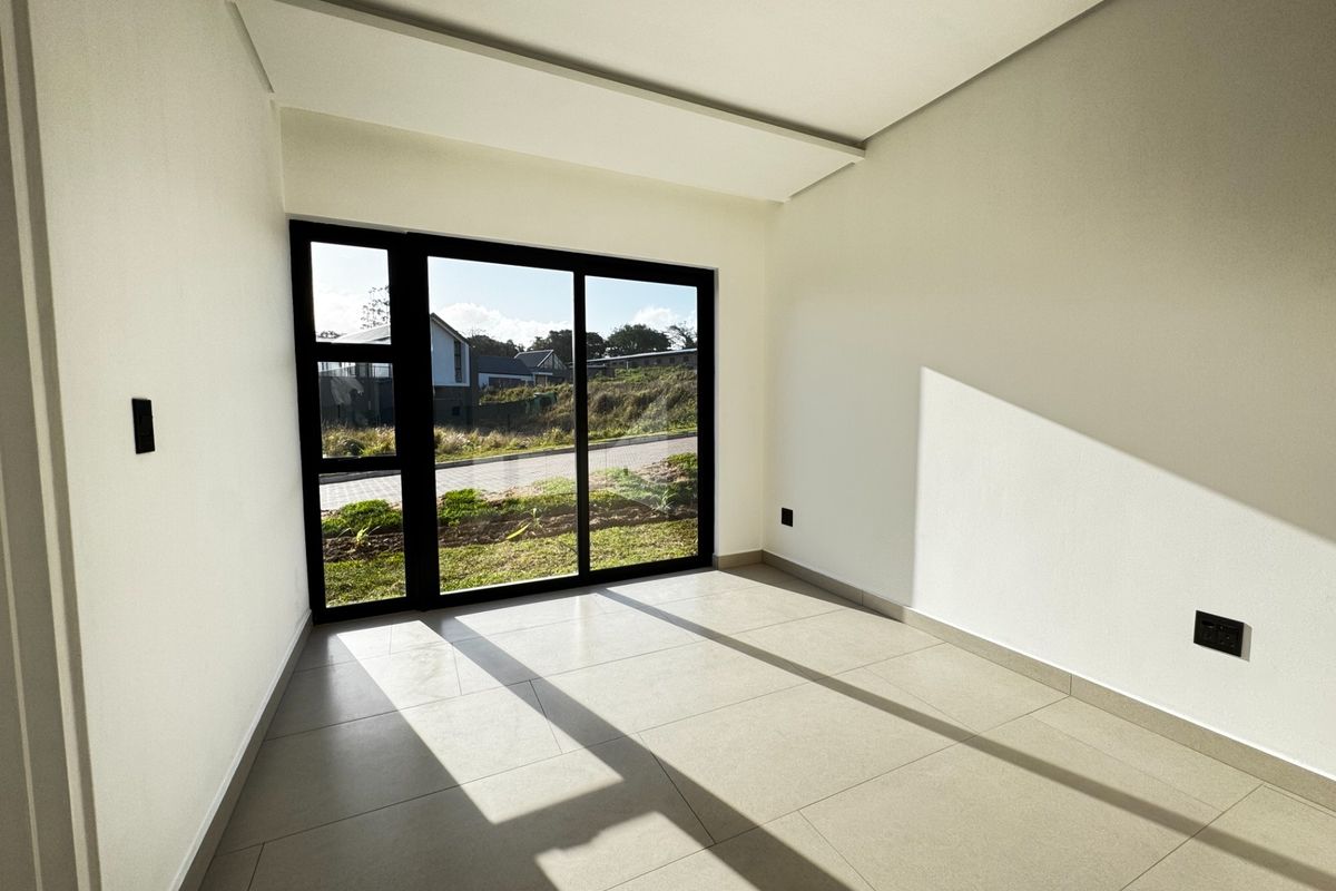 A bright, empty bedroom featuring modern tiled flooring and a large sliding glass door that provides natural light and outdoor access.