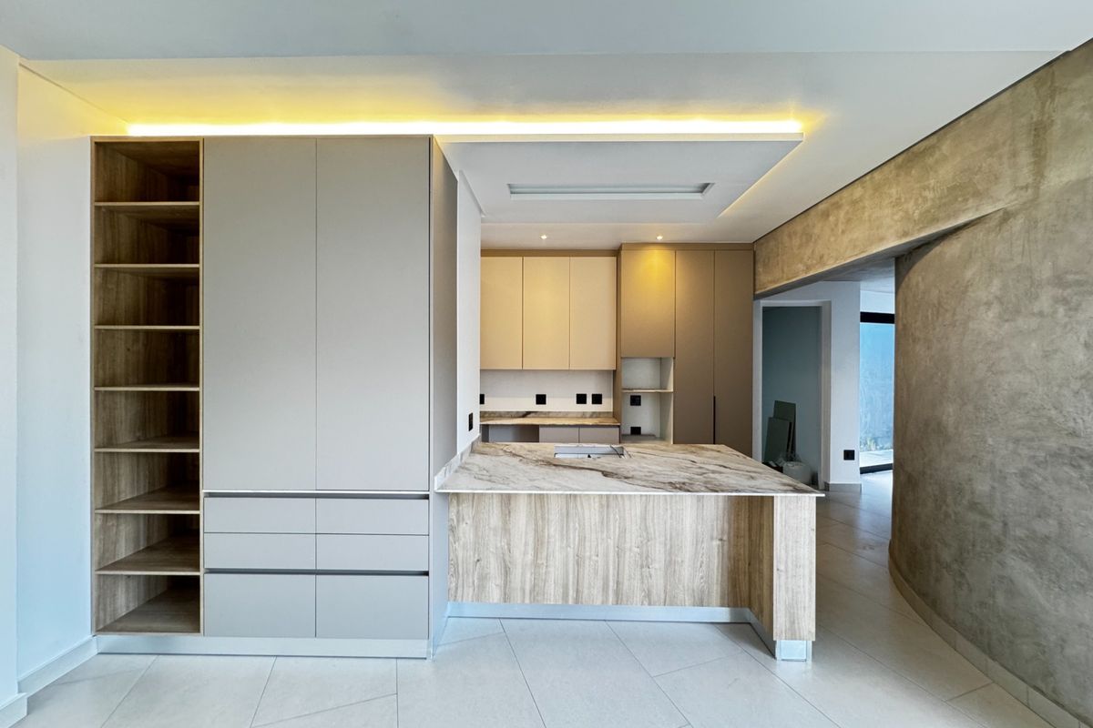 Modern kitchen featuring sleek built-in cabinetry, a stone-topped island, recessed ceiling lighting, and a striking concrete feature wall with neutral tiled flooring.