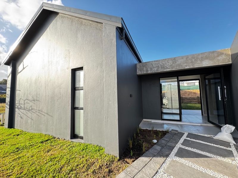 Modern rear exterior view featuring a grey facade, sliding glass doors leading to a paved patio, and a well-maintained garden area.
