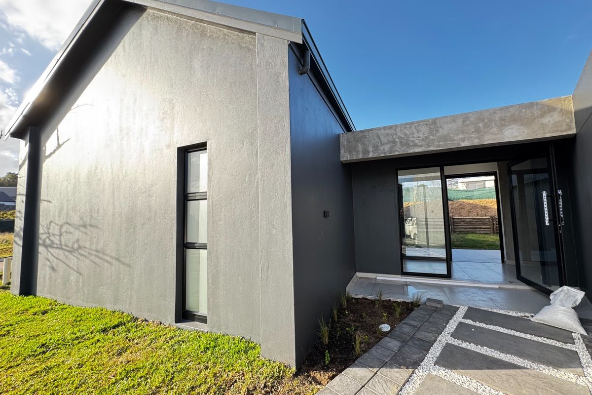 Modern rear exterior view featuring a grey facade, sliding glass doors leading to a paved patio, and a well-maintained garden area.