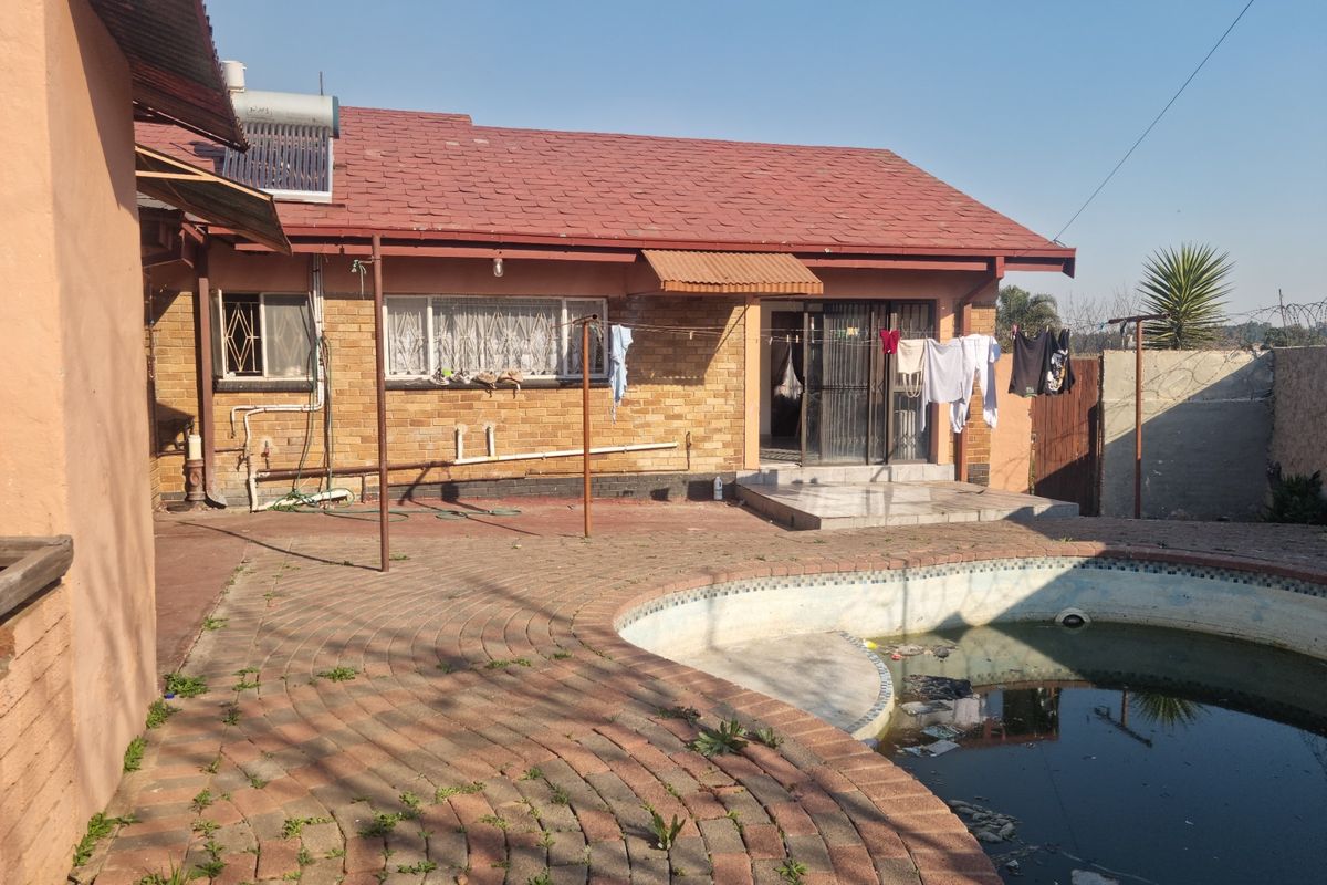 Rear exterior view of a brick house featuring a paved patio area and a swimming pool requiring maintenance.
