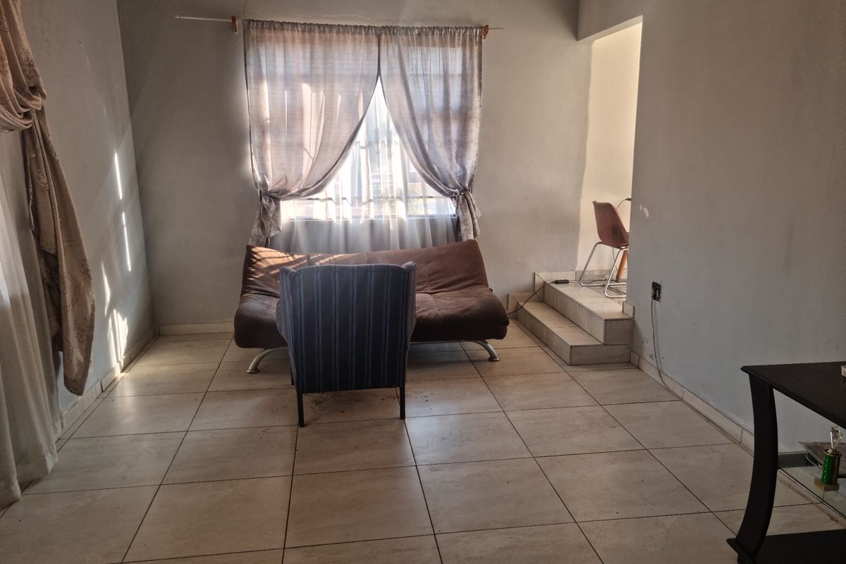 A living room area featuring tiled flooring and a raised platform section, providing a functional space with potential for cosmetic updates.