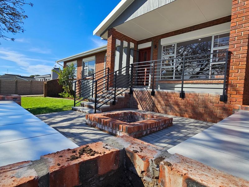 Front exterior view featuring a brick facade, paved patio area with a built-in brick fire pit, and metal safety railings leading to the entrance.
