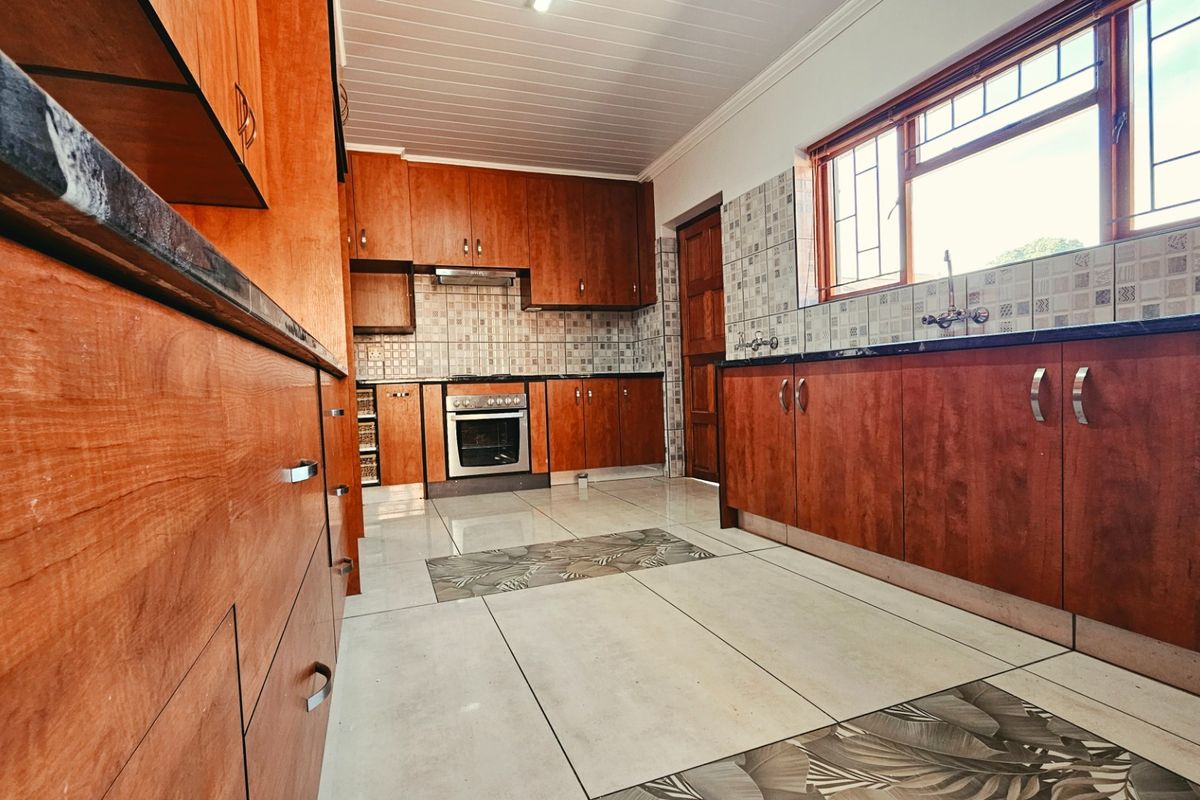 A spacious kitchen featuring warm-toned wooden cabinetry, granite countertops, built-in oven, extractor fan, and tiled flooring with a decorative inlay.