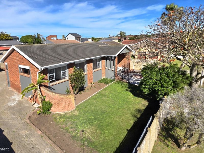 Aerial view of a single-story brick house featuring a tiled roof, paved driveway, and a well-maintained front lawn.
