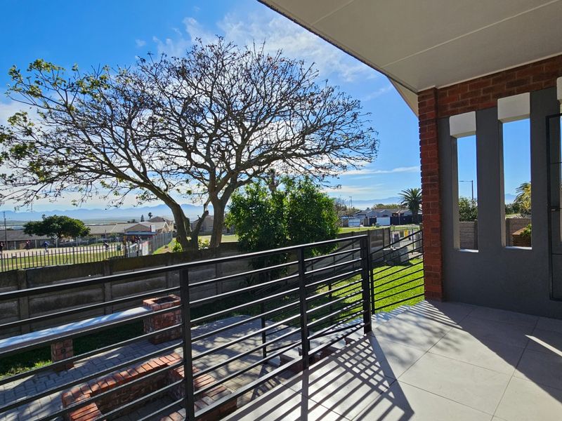 A covered patio featuring tiled flooring, a metal balustrade, and a built-in brick braai, offering an open view of the surrounding neighborhood.