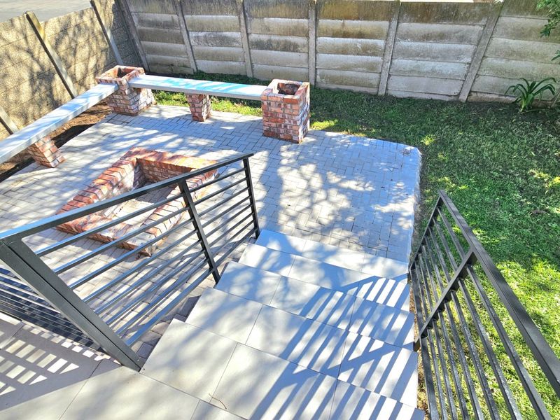 Outdoor patio area featuring a built-in brick fire pit, integrated brick seating, paved flooring, and modern metal railings leading down from the main dwelling.