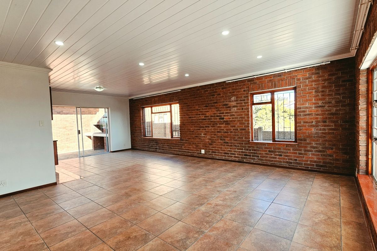 Spacious living area featuring exposed brick walls, tiled flooring, recessed lighting, and large windows, providing a bright and open atmosphere.