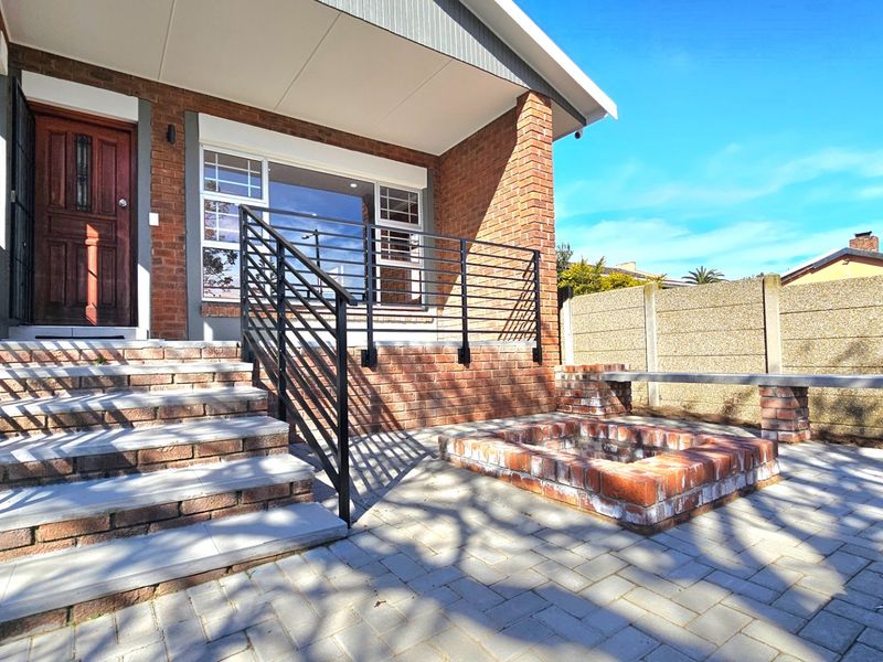 A well-maintained outdoor patio area featuring brick paving, a built-in brick fire pit, and concrete steps leading to the main entrance.