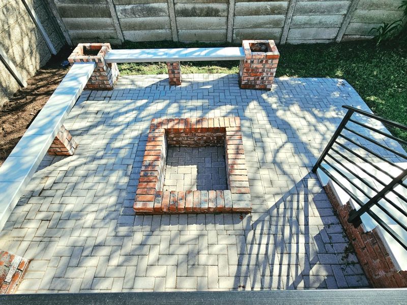 An outdoor patio area featuring a built-in brick fire pit and integrated brick bench seating, set within a paved courtyard with boundary walling.