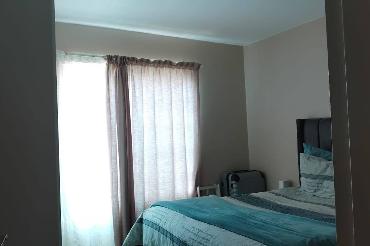 A bedroom featuring neutral wall tones and natural light filtered through window curtains.