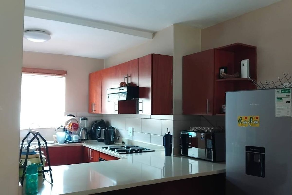 A functional kitchen featuring laminate cabinetry, stone countertops, a built-in hob with extractor fan, and a tiled backsplash.