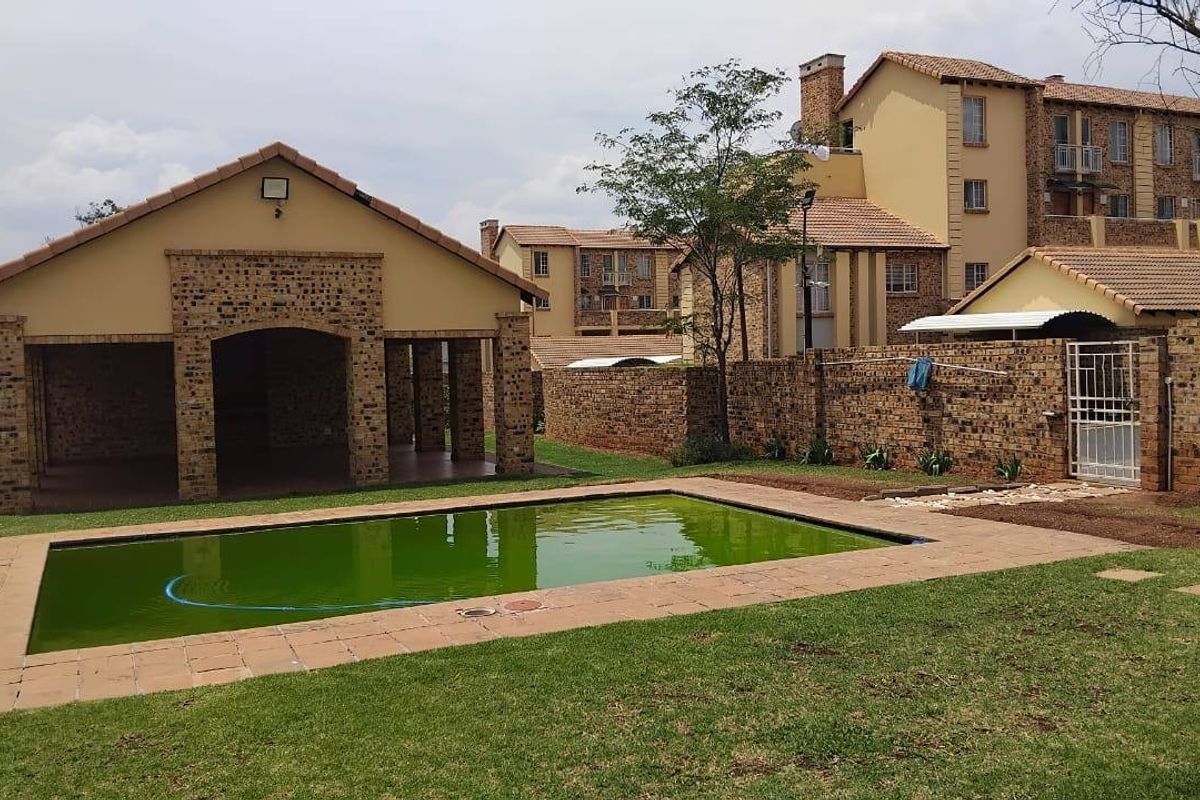 Outdoor pool area featuring a swimming pool, brick perimeter wall, and a covered patio structure within a residential complex setting.